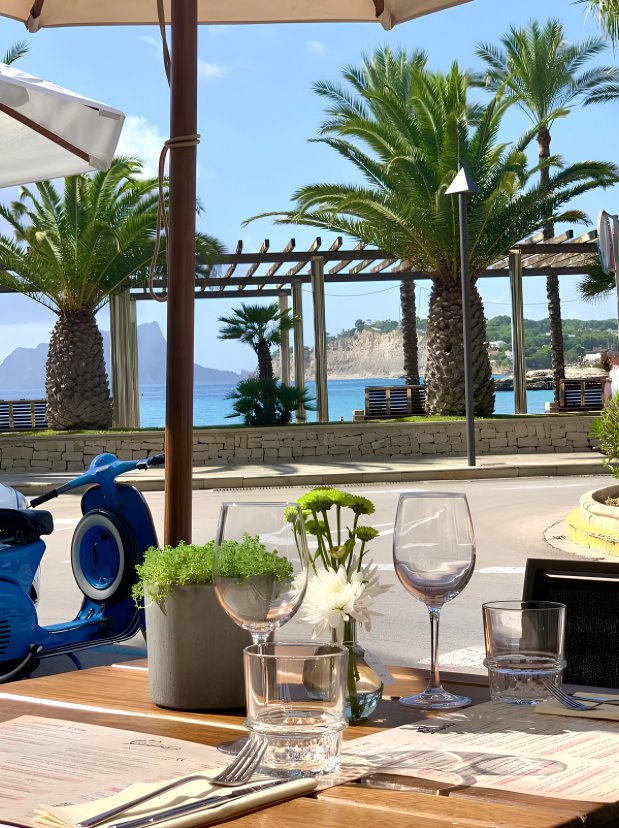 A table at Restaurante Vespaz with Moraira sea view, palm trees and a Vespa